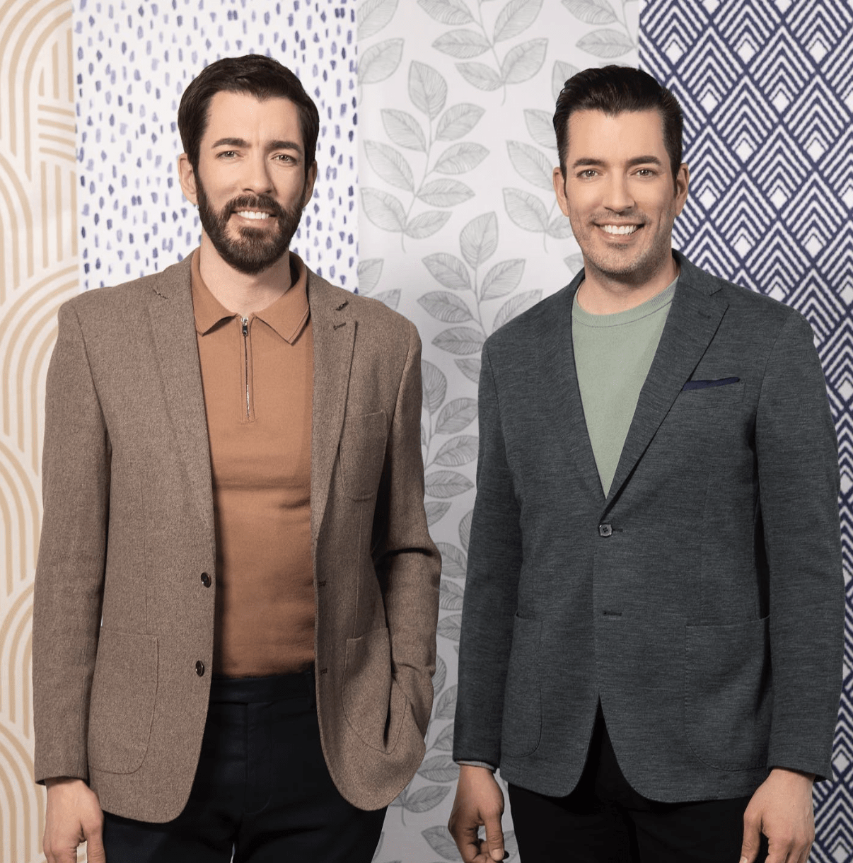 drew and jonathan scott property brothers standing in front of wallpaper wearing suits