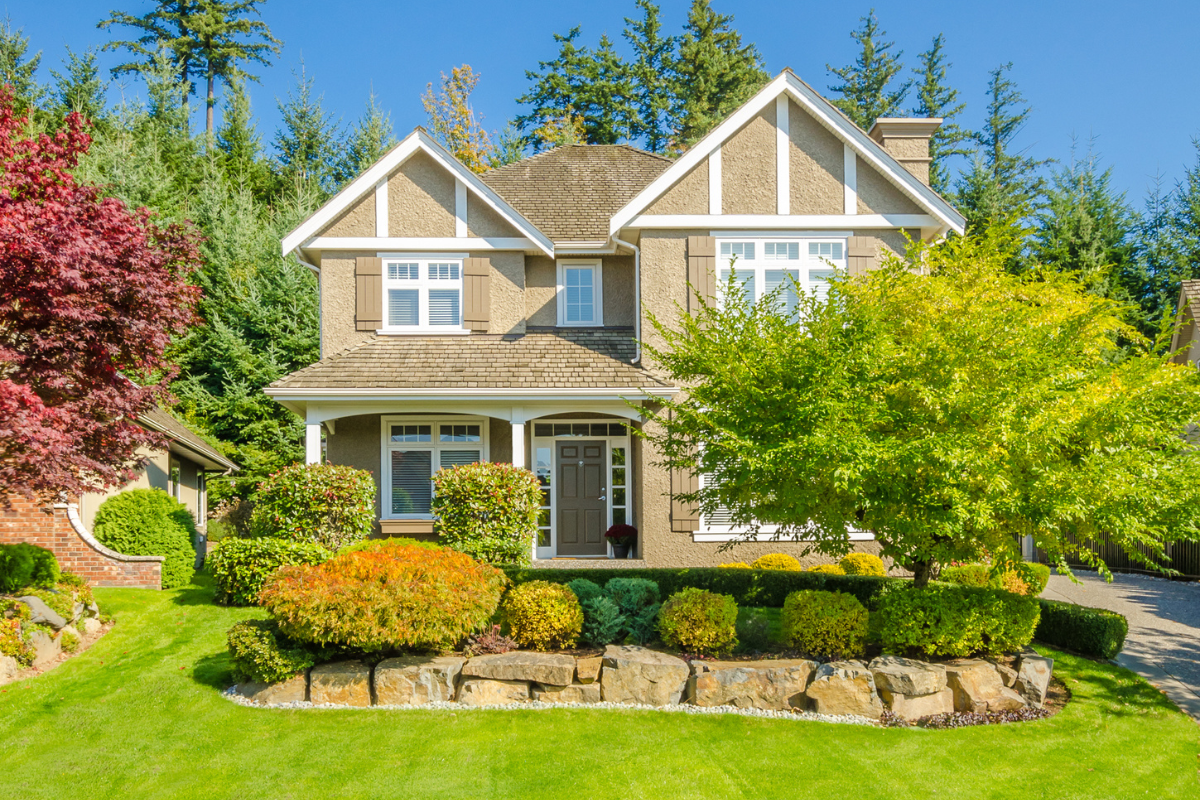 front of large house tan stone edge garden green grass trees