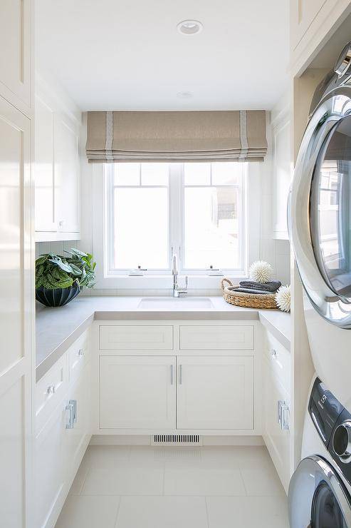 u shape small laundry room large natural light window tan roman shade stacked washer and dryer white shaker cabinets