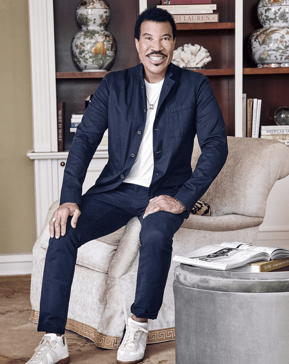 lionel ritchie sitting on a velvet chair in a blue suit