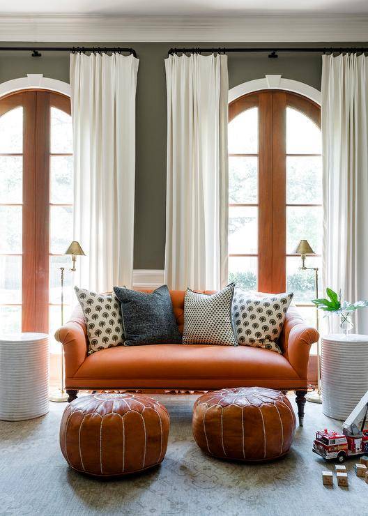 orange couch in front of curved windows white curtains throw pillows ottomans