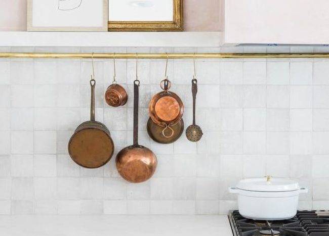 gold rod with hanging copper pans white tile kitchen backsplash modern art cabinetry stove