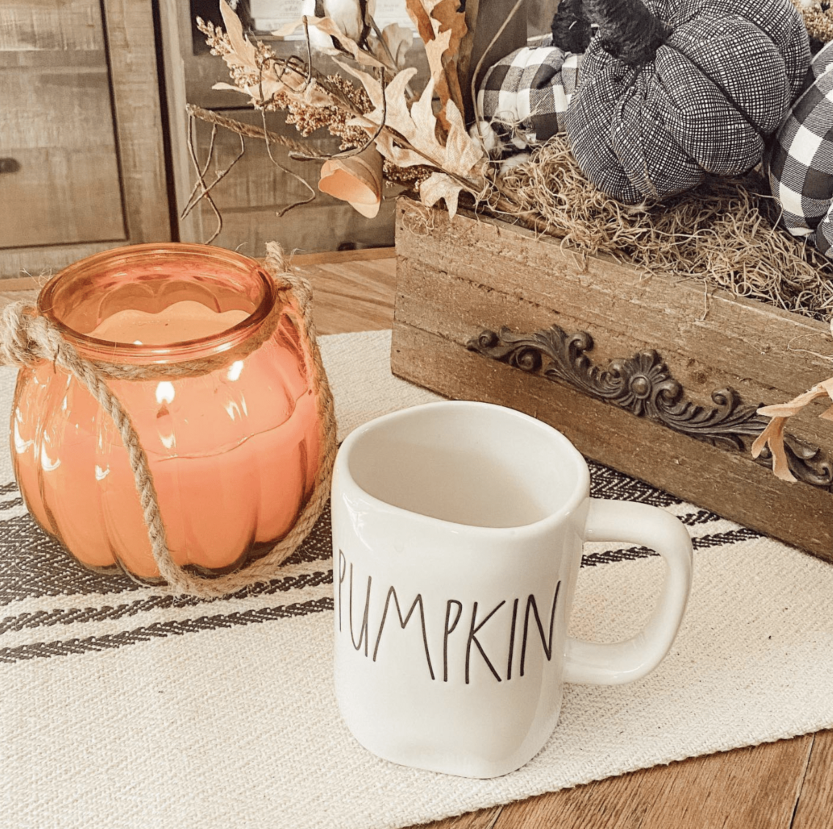 glass pumpkin candle on coffee table with rae dunn mug and buffalo check pumpkin