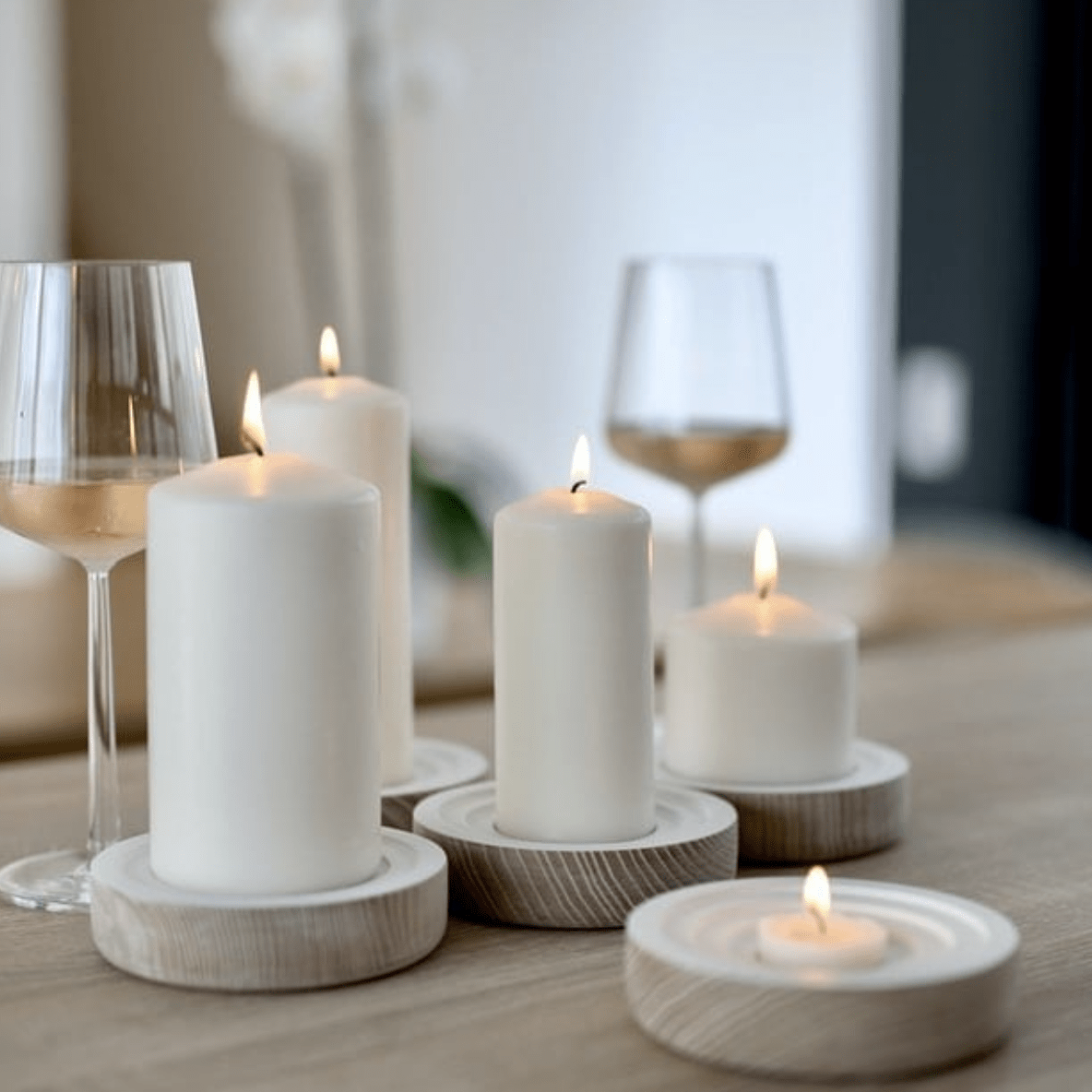 simple white candles on neutral white wood stands wine glasses