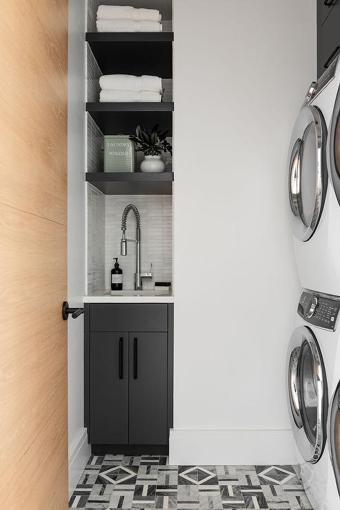 geometric floor tiles stacked white washer and dryer slender small sink black cabinetry white towels countertop pull down faucet laundry room.