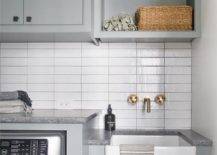 small white apron sink laundry room gold wall mounted faucet tile backsplash light gray cabinetry seagrass baskets