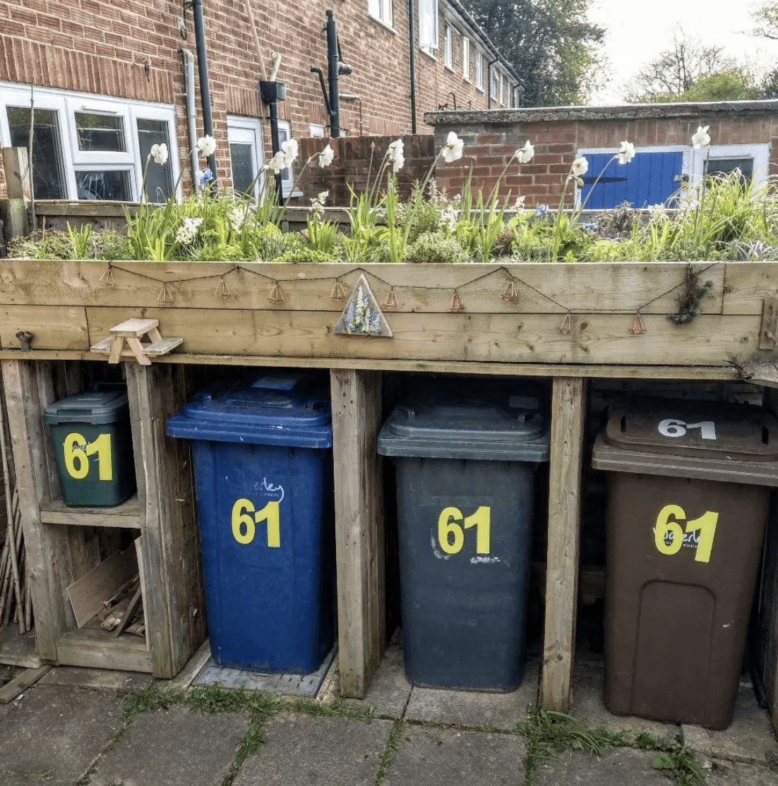 raised garden bed above trash containers concrete patio with houses in background