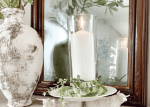 white candle holder with highland bulls pillar candles on table with mirror behind and rustic vase