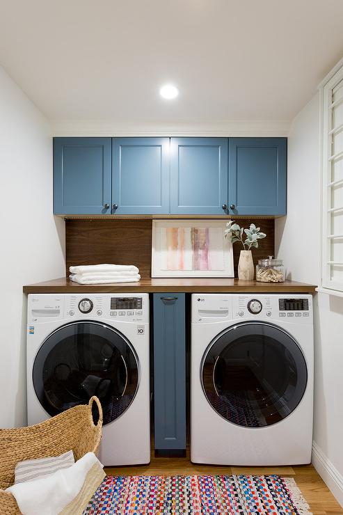 blue shaker cabinetry small laundry room white front load washer and dryer colorful rug wood countertop