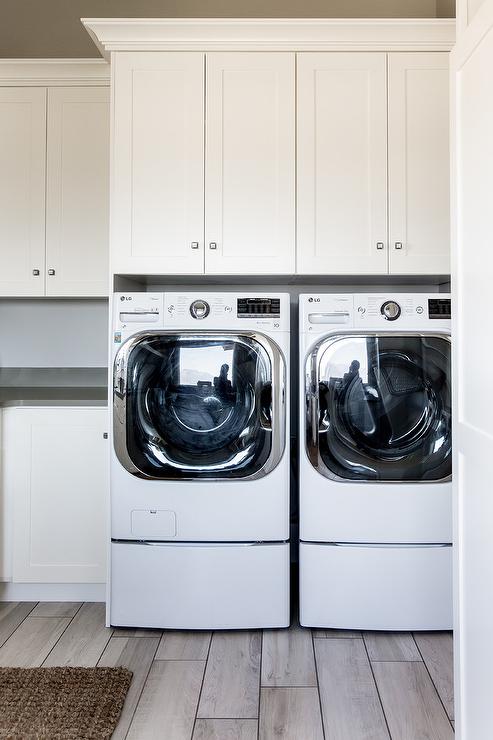 white shaker cabinets over front load washer and dryer pair wood tile floor