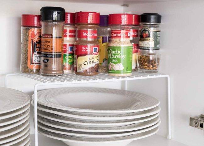 wire shelf riser inside cupboard white plates underneath spices on top