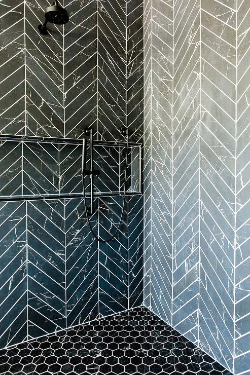 Black hexagon floor tiles complement black chevron shower surround tiles holding a matte black shower head over a long chevron tile