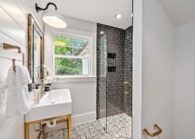 A white and gold sink with a brass base featuring a satin nickel faucet and a smoke gray tiled mirror white vintage barn sconce mounted on shiplap walls in a modern farmhouse bathroom design
