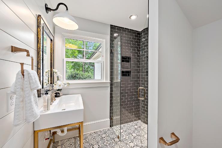 A white and gold sink with a brass base featuring a satin nickel faucet and a smoke gray tiled mirror white vintage barn sconce mounted on shiplap walls in a modern farmhouse bathroom design