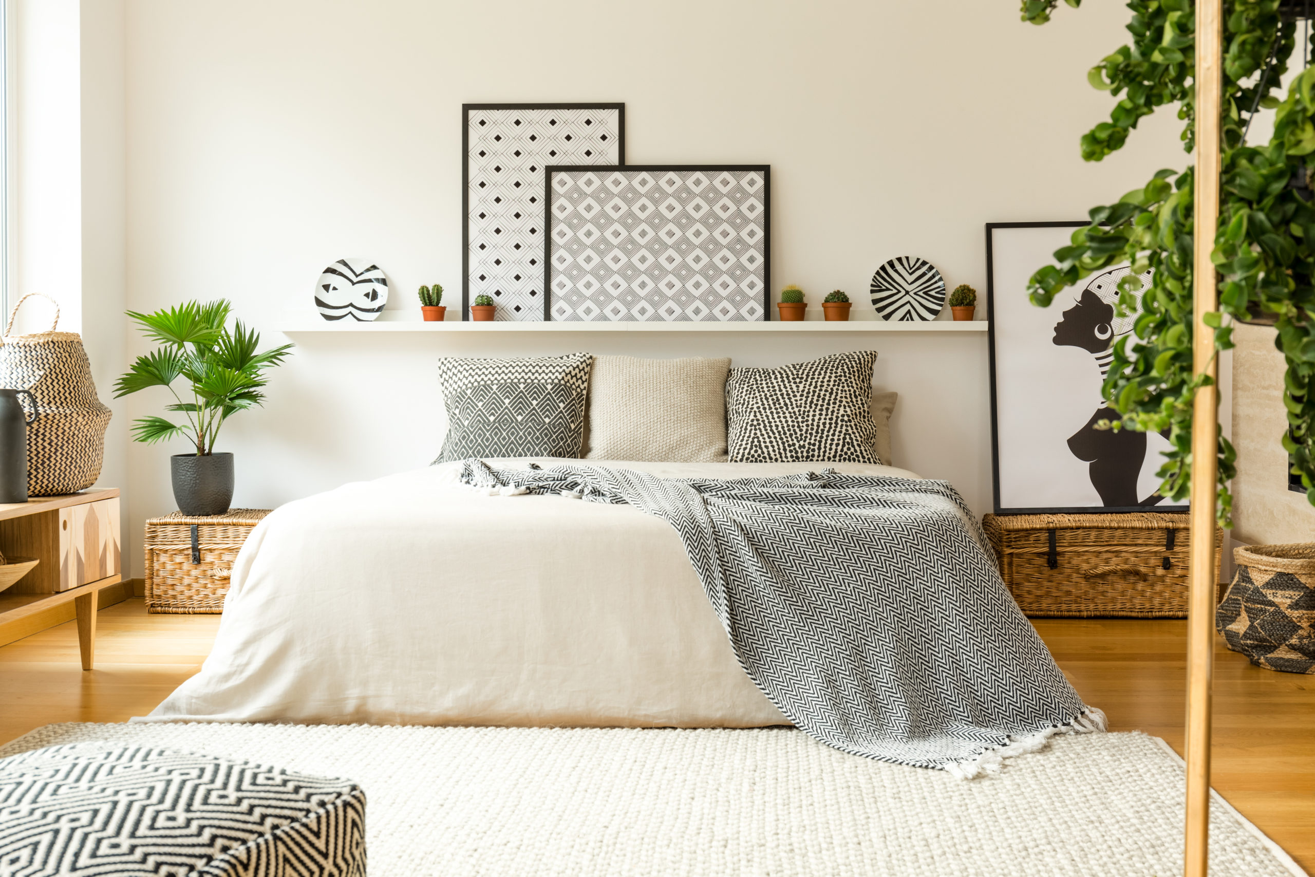 Warm bedroom interior with a comfy bed, patterned blanket and pillows, plants and modern graphics