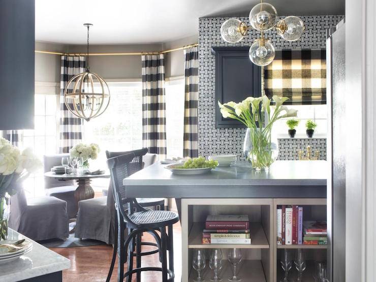 breakfast nook features a bay window dressed in black and white striped curtains filled with a round dining table lined with gray slipcovered dining chairs illuminated by an orb chandelier