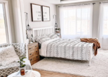 white modern farmhouse boho style bedroom bed geometric bedding accent chair and farmhouse signs hanging above bed