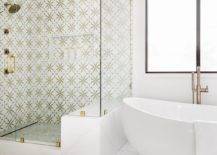 Seamless glass walk-in shower is clad in marble and brass mosaic surround tiles and is finished with a niche. A oval freestanding bathtub is located beside the shower and beneath a window.