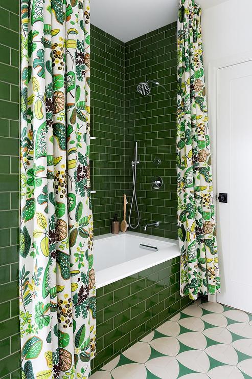 A green subway tiled drop-in bathtub is covered with 2 white and green shower curtains and fitted with a white quartz deck fixed against glossy green surround tiles.