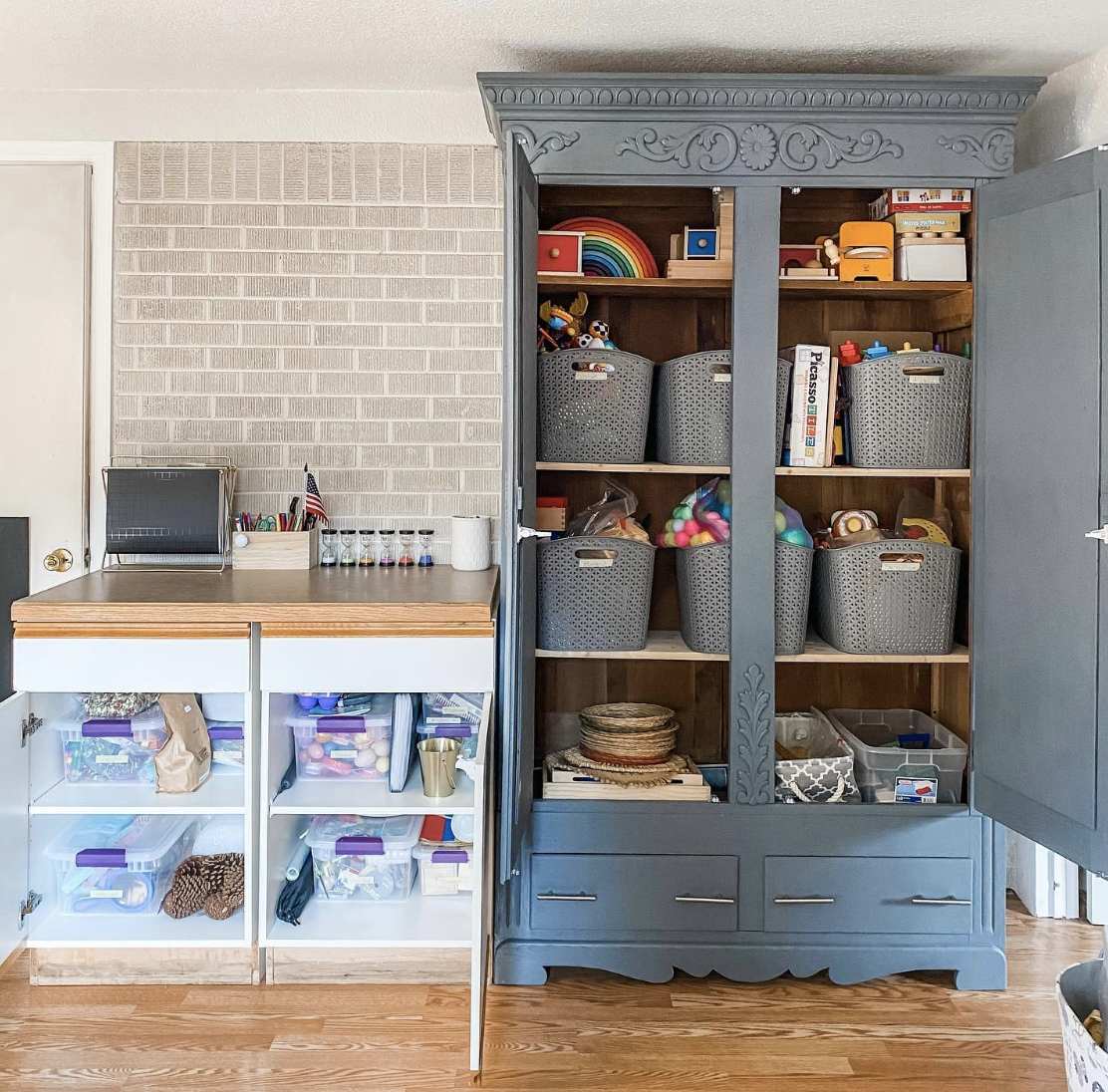 blue tall cabinet filled with totes and baskets for hidden toy storage brick wall background white smaller cabinet beside