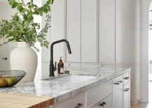 White kitchen island contrasted with matte black pulls features a butcher block and marble countertop holding a sink beneath a matte black faucet.