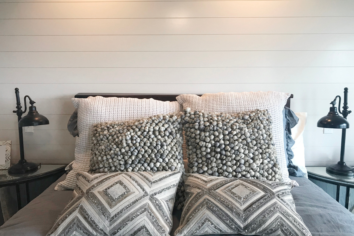 close up of farmhouse bed with decorative throw pillows and two black farmhouse lamp shade bedside lamps