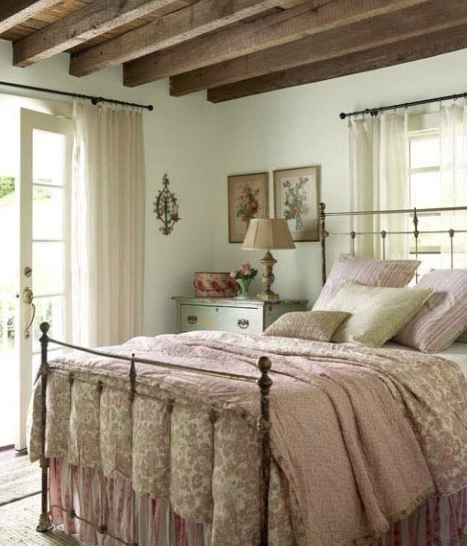 cozy cottage country farmhouse bedroom with floral bedding and bed skirt faux wood beams in ceiling wrought iron antique bed