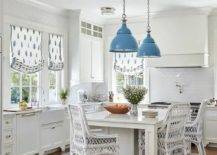 Blue industrial lanterns sconces hang over white island with wicker stools cabinetry kitchen