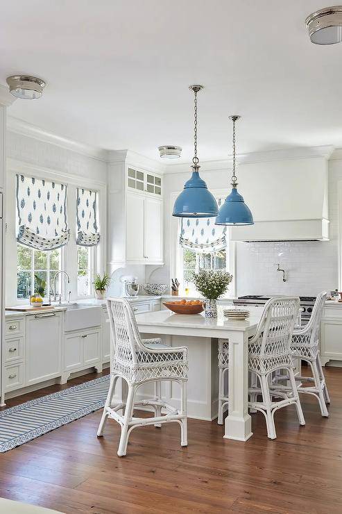 Blue industrial lanterns sconces hang over white island with wicker stools cabinetry kitchen