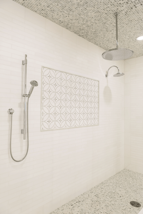 white linear tile surround in shower accented with decorative inset tiles hand held shower head to the left and wall-mounted rain shower head to right alongside a rain shower head mounted on mosaic marble tiled shower ceiling over a mosaic marble tiled floor