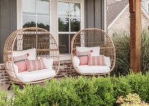 rattan chairs sit side-by-side on a covered front porch complementing a black cottage home