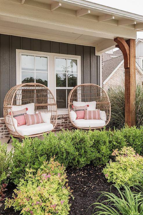 rattan chairs sit side-by-side on a covered front porch complementing a black cottage home