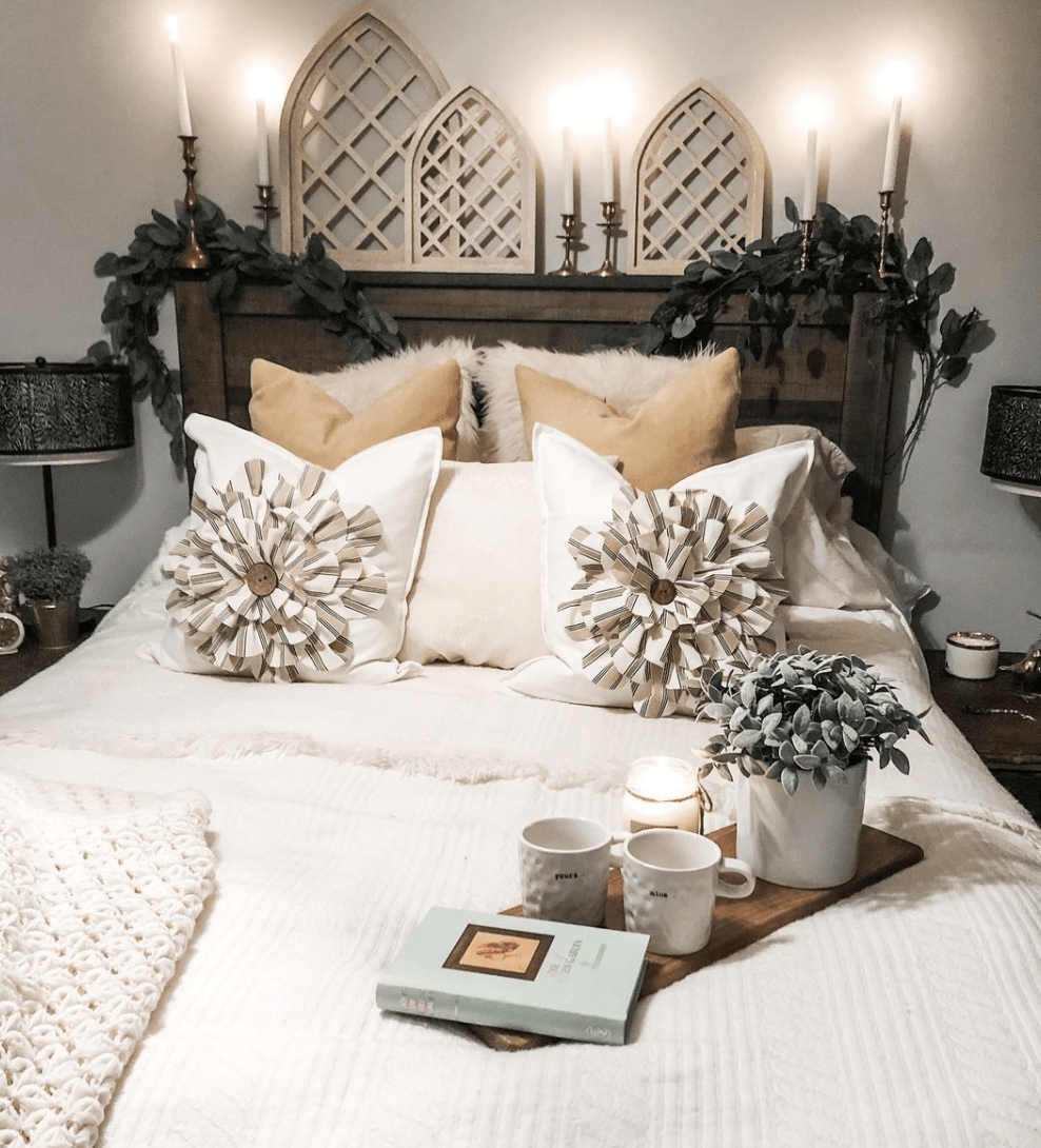 rustic wood farmhouse bed with decorative throw pillows book and white blankets greenery and gold candlesticks