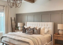 tufted white bed against sage green board and batted wall in farmhouse bedroom beaded chandelier wood primitive bench faux wood beams