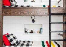 Farmhouse bunk room feature pipe plumbing railing and ladders on dark stained oak wood built-in bunk beds. Black and white plaid bedding mismatch with checkered sheets to create an diverse but stylish look in this shared space. Shiplap trim, wall shelf niches and black sconces complete the styled boys cottage bedroom.