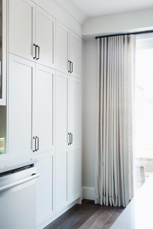 floor to ceiling white canvas curtains on black curtain rod with white shaker cabinetry and dishwasher