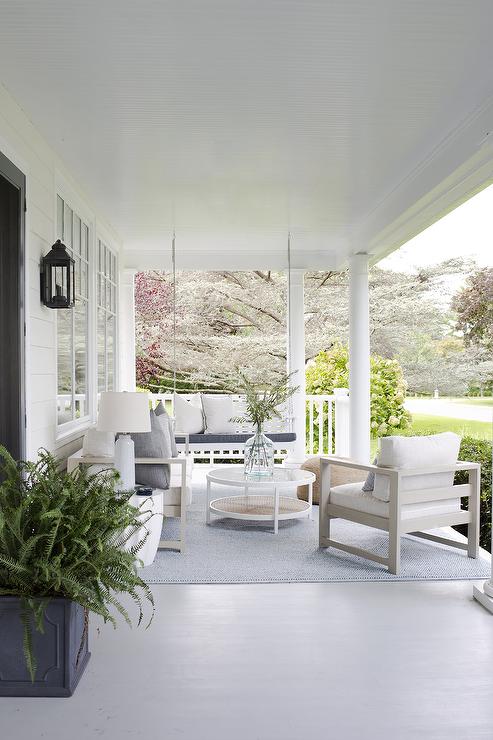 large view of front porch with white sitting chairs coffee table outdoor rug and fern in pot