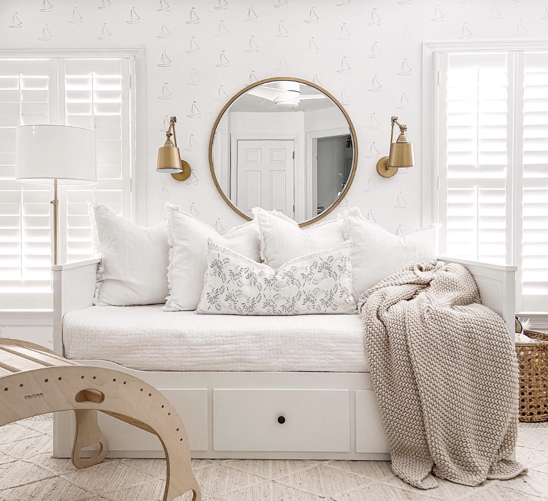 white day bed with drawers underneath for hidden storage white sailboat wallpaper with large round mirror gold wall sconce on either side