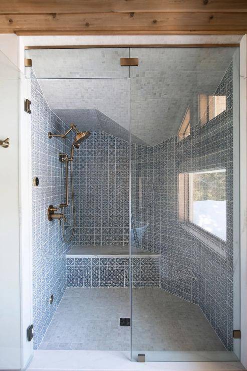 Bathroom features a walk-in shower that boasts blue mosaic Spanish tiles with a brass shower kit, a built-in tiled bench and a marble tiled ceiling.