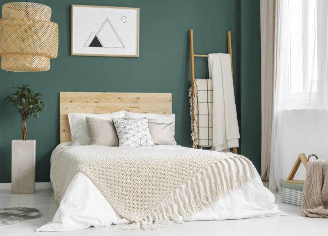 Plant and rattan lamp in green cozy bedroom interior with wooden bed against the wall with poster