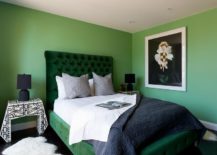 contemporary green and black bedroom stands out with green walls and a green velvet tufted sleigh bed dressed in white and black bedding topped with gray pillows. The bed is flanked by black and white bedside tables illuminated by black lamps.
