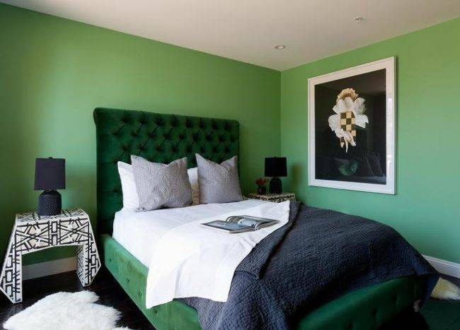 contemporary green and black bedroom stands out with green walls and a green velvet tufted sleigh bed dressed in white and black bedding topped with gray pillows. The bed is flanked by black and white bedside tables illuminated by black lamps.