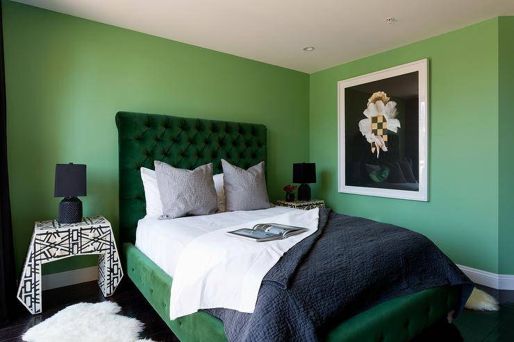 contemporary green and black bedroom stands out with green walls and a green velvet tufted sleigh bed dressed in white and black bedding topped with gray pillows. The bed is flanked by black and white bedside tables illuminated by black lamps.