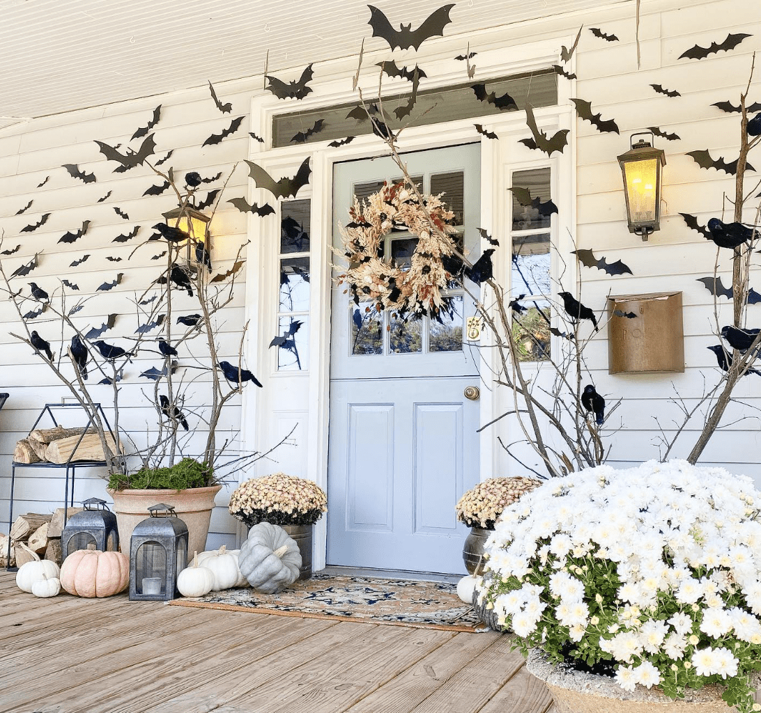 black bats on front porch across blue door white sided house pumpkins and white fall mums