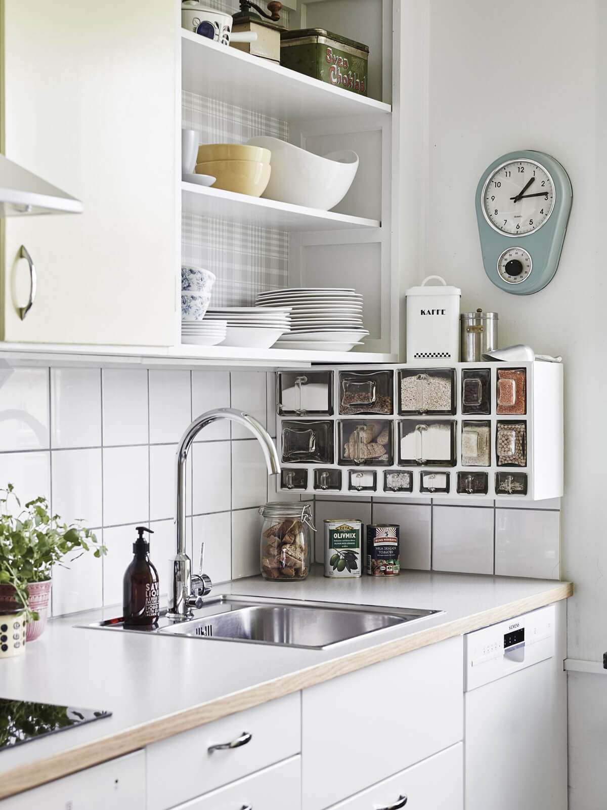 white kitchen with open shelving hanging storage boxes wall clock stainless steel sink