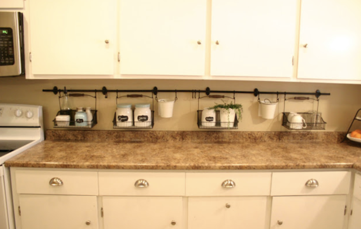 white kitchen cupboards with laminate countertops hanging black rod under cupboards with wire baskets