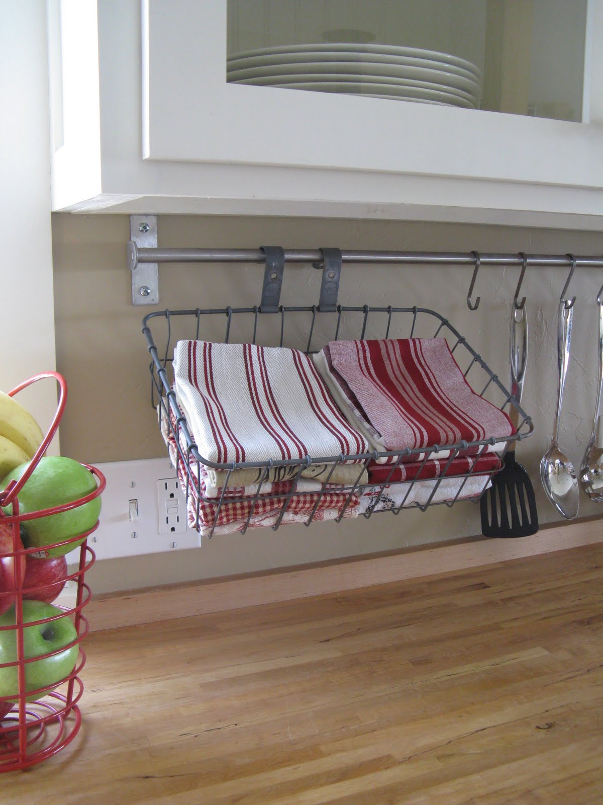 upcycled bicycle basket being used under kitchen cupboard with red dish towels inside