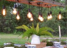 edison bulbs hanging from ladder chandelier outside above dining table with bowls and napkins