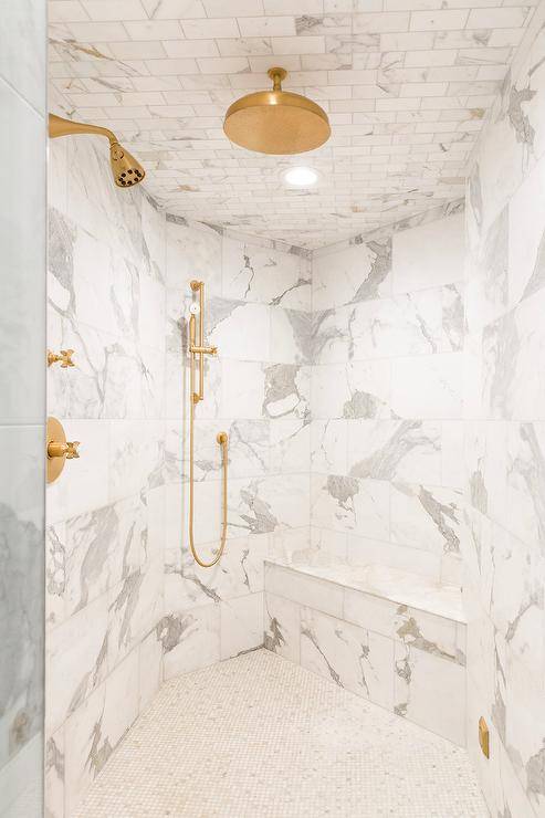 brass rain shower kit fixed to marble subway ceiling tiles over marble lattice floor tiles fitted in a curved walk-in shower
