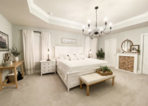 large white master farmhouse bedroom with black chandelier large white bed bench fireplace with wood rounds
